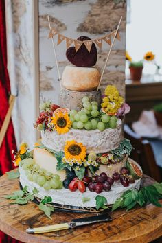 a multi layer cake with grapes, sunflowers and cheese on top is sitting on a wooden table