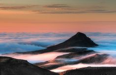 the mountains are covered in clouds as the sun sets over them and there is no image to describe