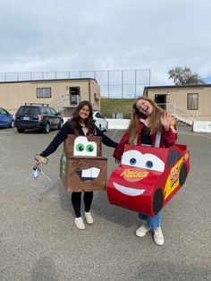 two girls dressed up as characters from the movie cars, one holding a paper bag and another carrying a cardboard box