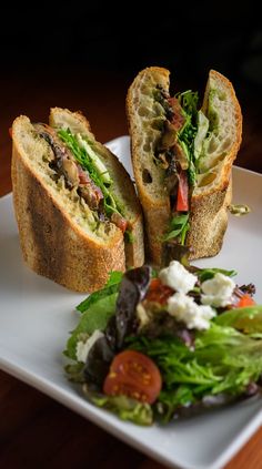 a sandwich cut in half sitting on top of a white plate next to a salad