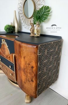 a wooden cabinet with black and gold designs on the front, next to a potted plant