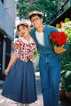 a man and woman standing next to each other in front of some buildings with flowers