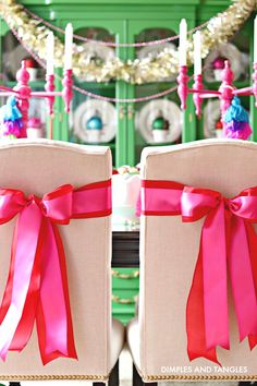 two chairs with pink bows on them are sitting in front of a christmas tree and garland