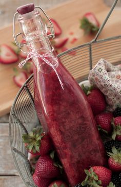 a glass bottle filled with liquid surrounded by strawberries