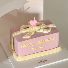 a pink birthday cake sitting on top of a white table next to a box with a candle