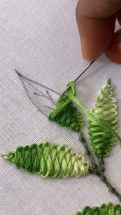 someone is working with some thread on the fabric to make something green and white that looks like leaves