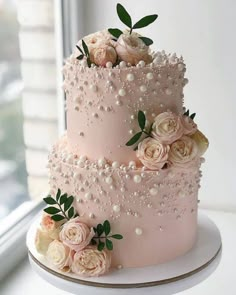 a three tiered cake with flowers and pearls on top is sitting in front of a window