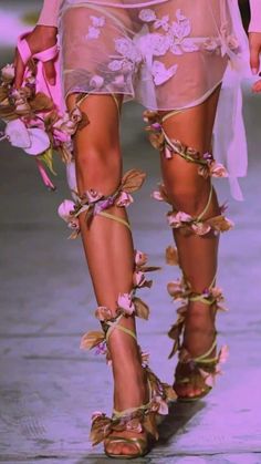 a woman walking down a runway wearing high heels and flowers on her leg, with one foot in the air