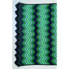 a green, blue and black blanket with fringes on the edges is hanging up against a white wall