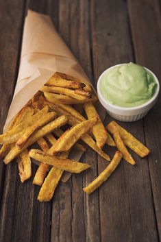 french fries with dip in the middle on wooden table next to paper wrapper and container