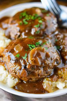 a white plate topped with meat and gravy covered in gravy on top of mashed potatoes