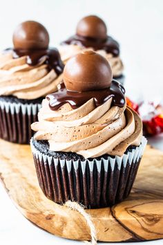 two chocolate cupcakes sitting on top of a wooden cutting board