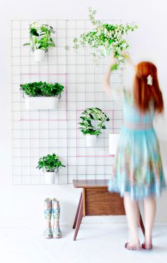 a woman standing in front of a wall with potted plants on top of it