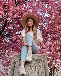 a woman sitting on top of a stone pillar in front of pink flowers and trees