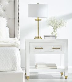 a white bed sitting next to a night stand with a lamp on top of it