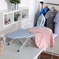 an ironing board sitting on top of a table next to a rack with clothes