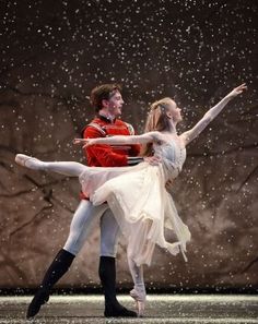 a man and woman in ballet clothes standing on stage with snow falling all around them