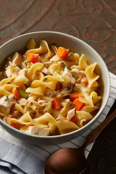 a bowl of chicken noodle soup on top of a blue and white towel next to a spoon