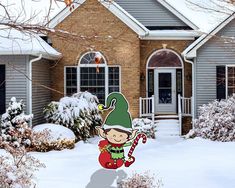 a house with snow on the ground and a christmas elf standing in front of it