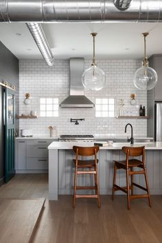 two wooden stools sit in front of an island with marble countertops and pendant lights