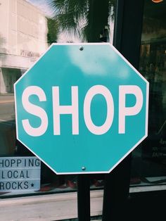 a blue stop sign sitting on the side of a road next to a store front