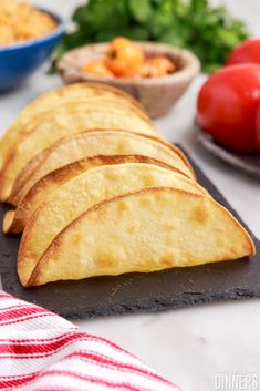 some tortilla chips are on a slate board next to tomatoes and lettuce