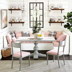 a dining room table with pink chairs around it and some shelves on the wall behind it