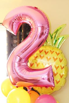 the number two balloon is next to some pineapples and other balloons in front of a mirror