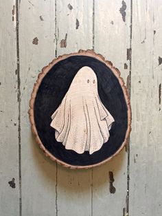 a wood slice with a ghost painted on it's face is hanging on the wall