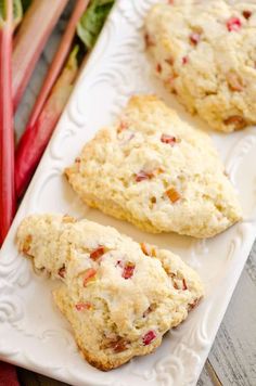 three scones sitting on top of a white plate next to rhubarb stalks