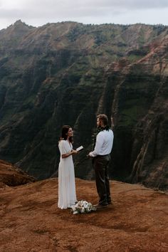 a man and woman standing on top of a mountain next to each other holding hands