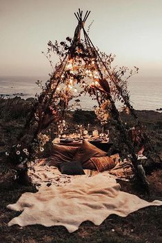 a teepee with lights and pillows on it near the ocean at sunset or dawn