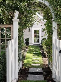 an open white gate leading to a house with a small garden in the front yard