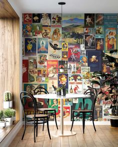 a dining room table with two chairs in front of a wall full of pictures and plants