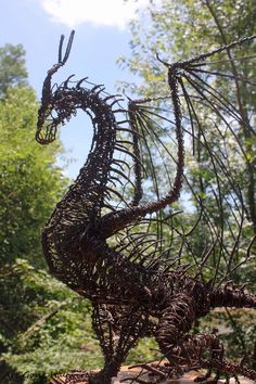 a wire sculpture of a dragon on top of a rock with trees in the background