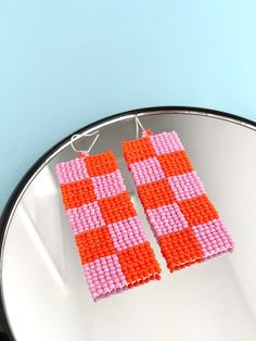 two pink and orange squares are hanging from a pair of earrings on a white plate