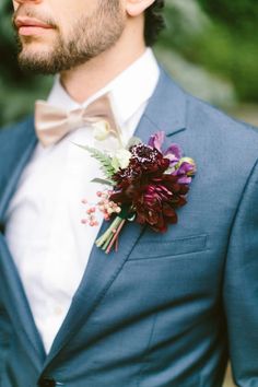 a man in a blue suit and bow tie wearing a flower boutonniere