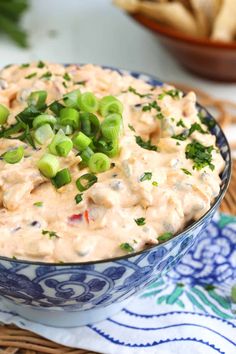 a bowl full of dip with green onions and celery on the side next to chips