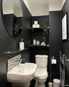 a white toilet sitting next to a bathroom sink under a round mirror in a black and white bathroom