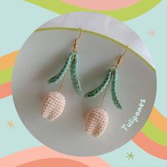 two crocheted earrings on a white plate with green leaves and pink flowers in the background