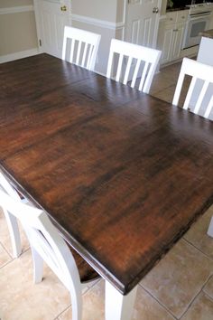 a large wooden table with white chairs around it in the middle of a tiled floored kitchen