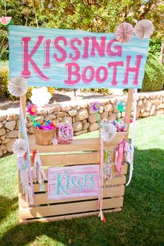 a sign that says kissing booth on top of a wooden crate with decorations around it