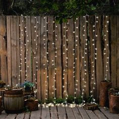 a wooden fence with lights hanging from it and potted plants on the ground next to it