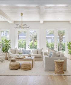 a living room filled with lots of furniture next to two large windows and potted plants