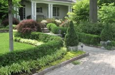 a house with lots of trees and bushes in front of it on a brick walkway