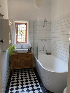 a white bath tub sitting next to a sink under a window in a tiled bathroom