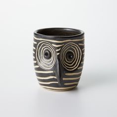 a black and white cup with an owl's face painted on the side, in front of a white background