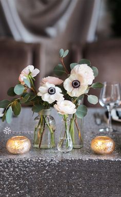 three vases filled with flowers sitting on top of a table next to wine glasses