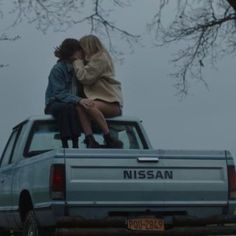 two people are sitting on the back of a pickup truck while one person is kissing