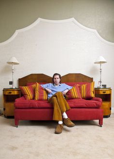 a man sitting on top of a red couch in front of a white headboard